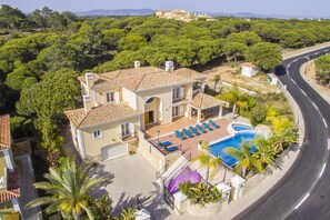 A two-story house with a swimming pool, surrounded by greenery and a curved road.