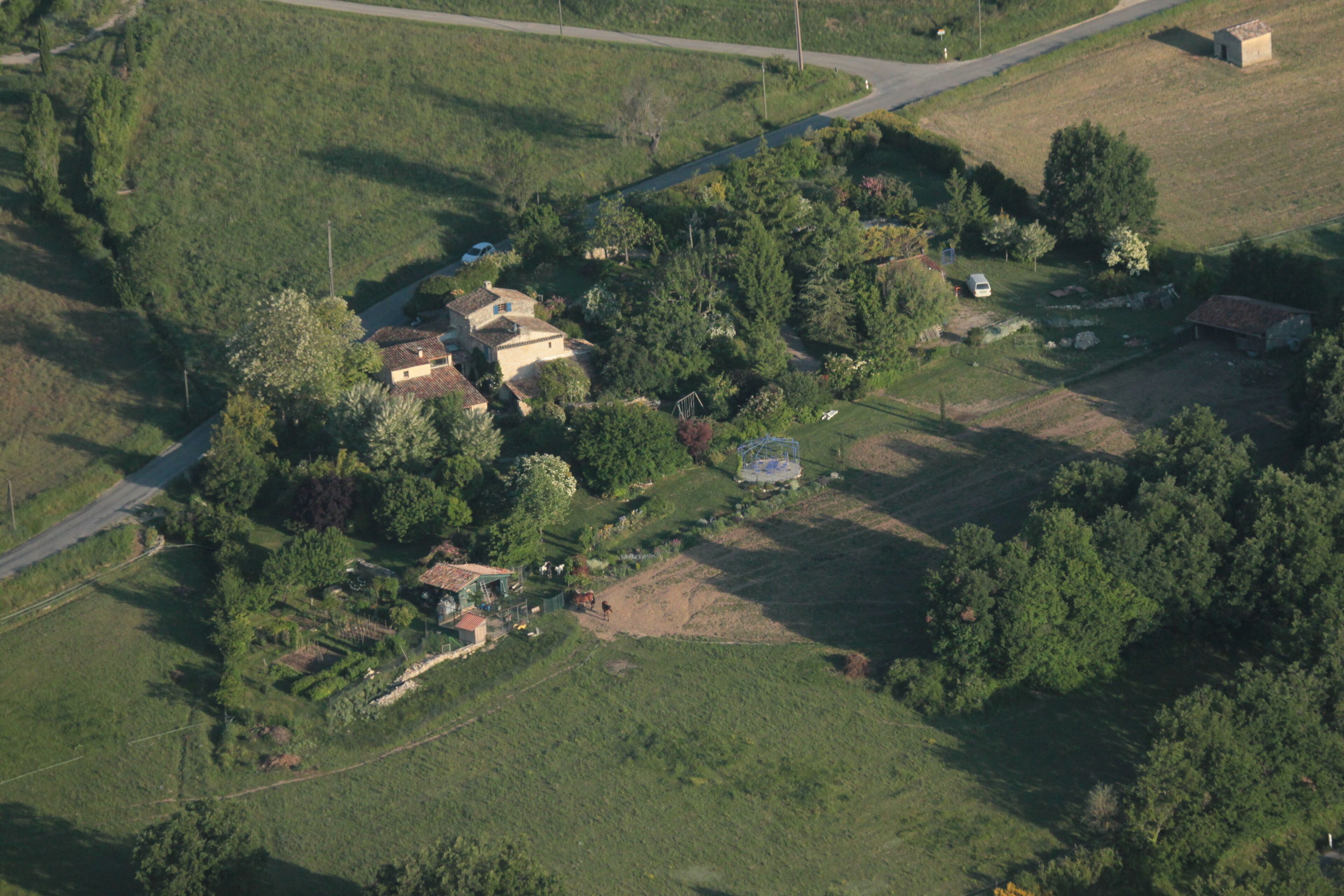 Vista aérea de una zona rural con casas dispersas, una pequeña masa de agua y una carretera.