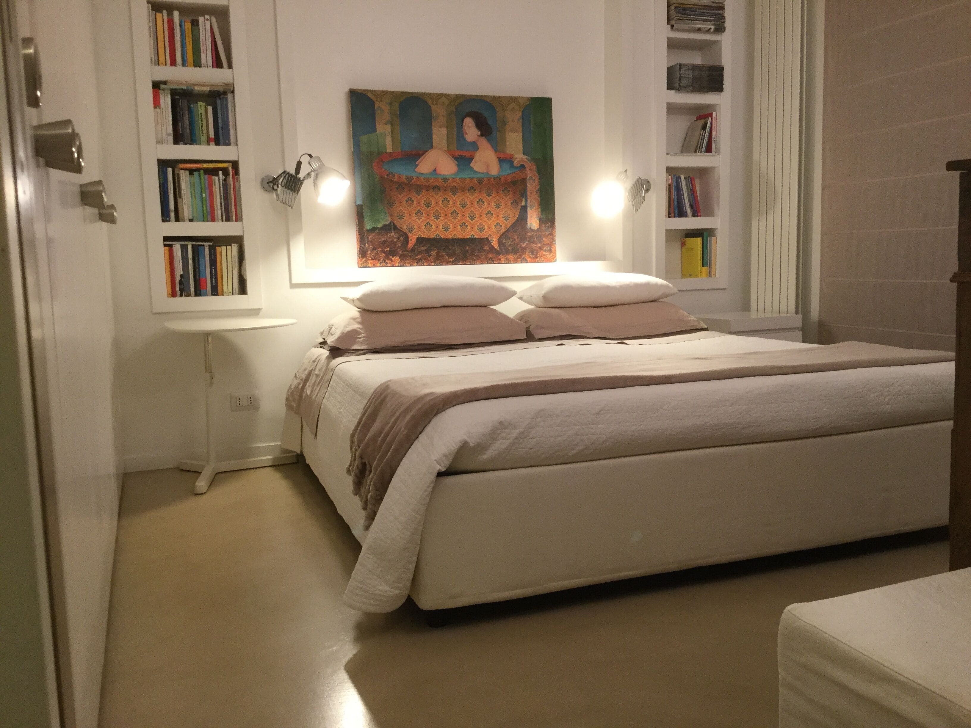 Une chambre à coucher avec un grand lit, une table de chevet, une lampe fixée au mur et une bibliothèque.