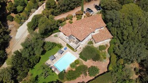 Eine Luftaufnahme eines Hauses mit einem Ziegeldach, einem Swimmingpool und umgebender Bepflanzung.