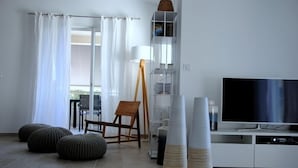 Ein modernes Wohnzimmer mit Flachbildfernseher, einem Holzstuhl, Poufs und einer weißen Kommode.