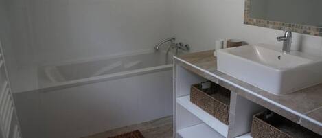 Un baño con bañera, lavamanos y espejo. Hay cestas de almacenamiento debajo del lavamanos y una alfombrilla de ducha en el suelo.