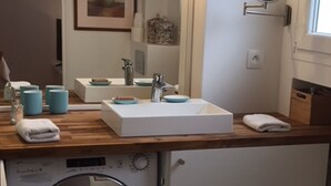 Ein kleines Badezimmer mit einer integrierten Waschmaschine, einem Waschbecken mit Spiegel und einem gerahmten Bild an der Wand.