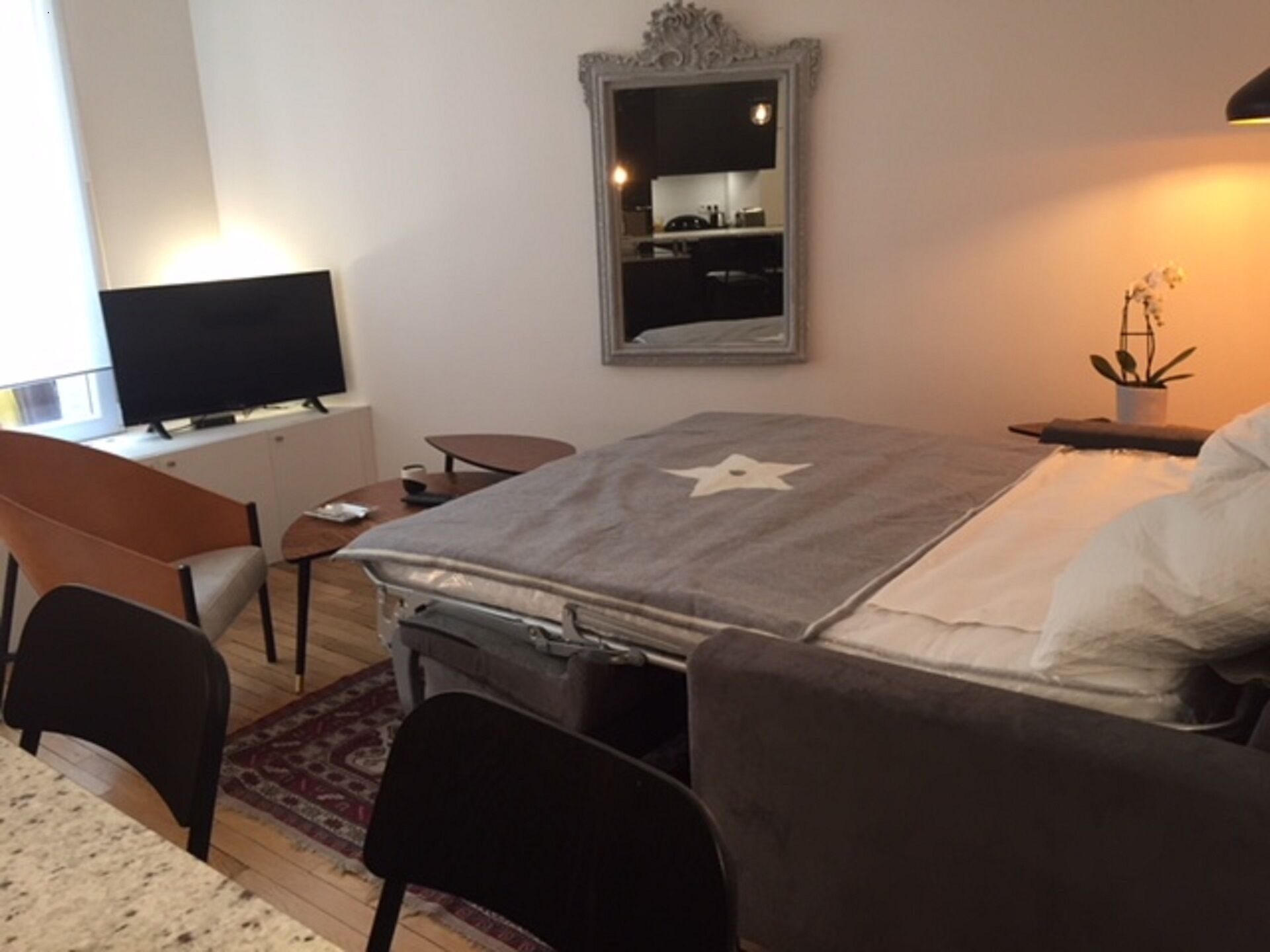 A hotel room with a bed, a desk, a chair, a TV, and a mirror.