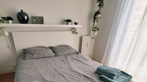 Siististi pedattu sänky, jossa on harmaat vuodevaatteet, valkoinen pääty ja pieni hylly koriste-esineille.