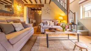 Ein gemütliches Wohnzimmer mit einer Holztreppe, einer Sterndeko und einem Couchtisch mit Blumen.