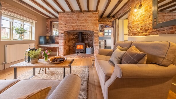Ein gemütliches Wohnzimmer mit Kamin aus Backstein, Holzbalken, einer Couch und einem Fernseher.