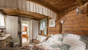 Una habitación acogedora con techo de madera, una cama con ropa de cama floral, un aparador y una silla.