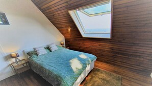 Ein Schlafzimmer mit Bett, Nachttisch, Lampe, Fenster und Blick zum Himmel.