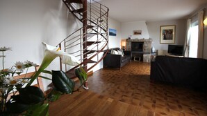 Ein geräumiges Wohnzimmer mit Holzdielenboden, einer schwarzen Couch, einem Kamin und einer Wendeltreppe.