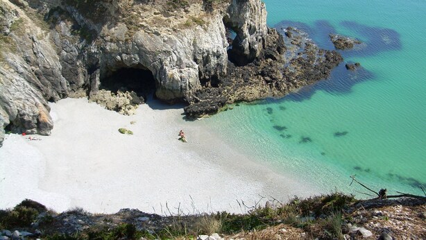 Eine Küstenlandschaft mit einem felsigen Klippen, einem Höhleneingang und einem Sandstrand.