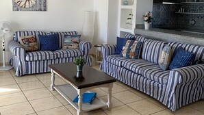 A living room with striped sofas, a coffee table, and a kitchen area with blue and white tiles. - Villa in Puerto del Carmen, Lanzarote, Canary Islands  (Tías)