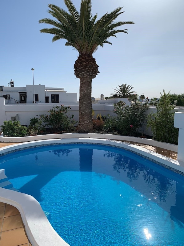 A swimming pool with a palm tree in the center, surrounded by white buildings. - Villa in Puerto del Carmen, Lanzarote, Canary Islands (Tías)