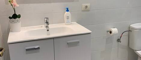 A bathroom with a white sink, mirror, and toilet. There is a trash bin and a blue towel hanging on the wall.