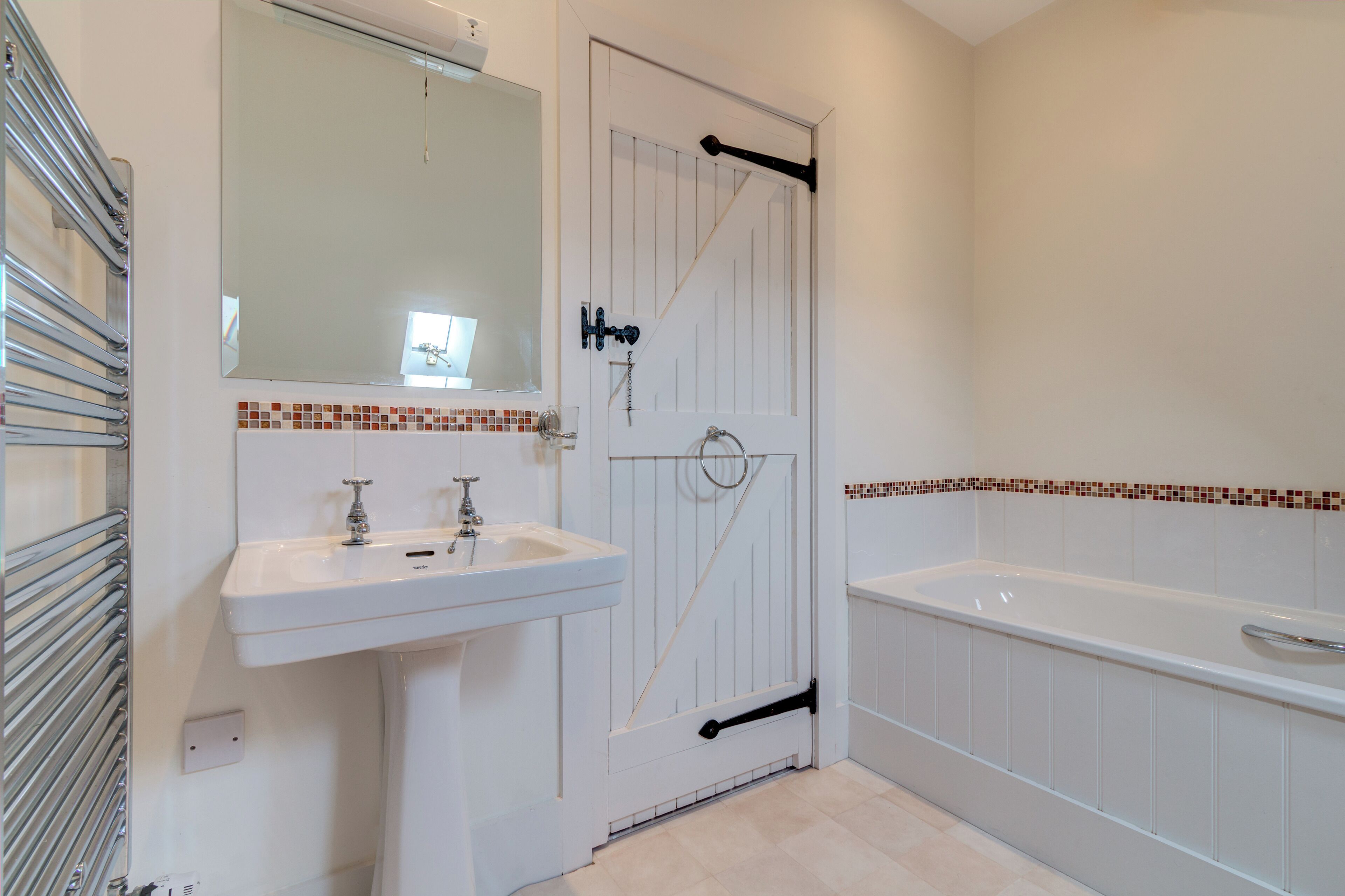 A bathroom with a white sink, a mirror, a door with a towel rack, and a bathtub.
