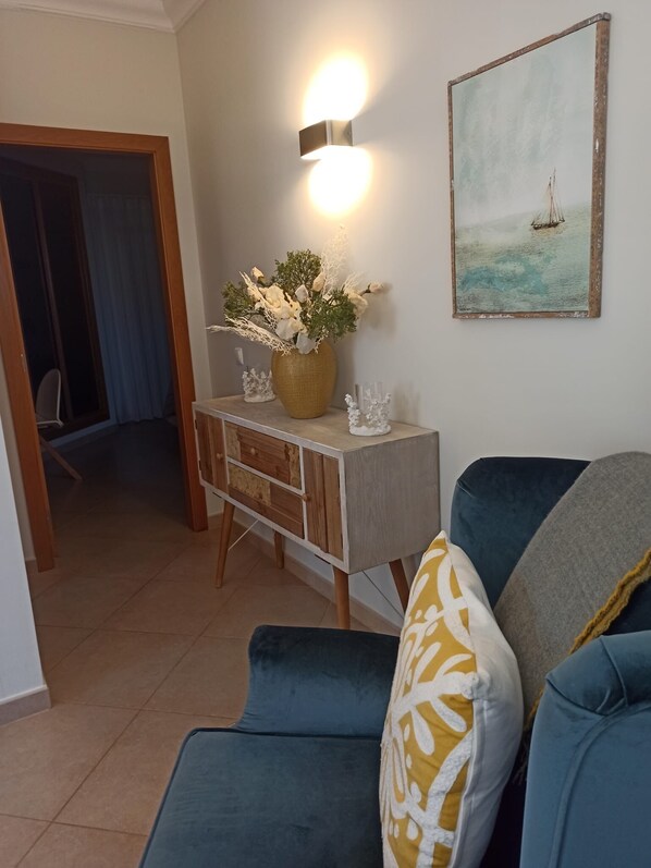 A living room with a blue sofa, a wooden cabinet with a vase of flowers, and a painting of a sailboat.