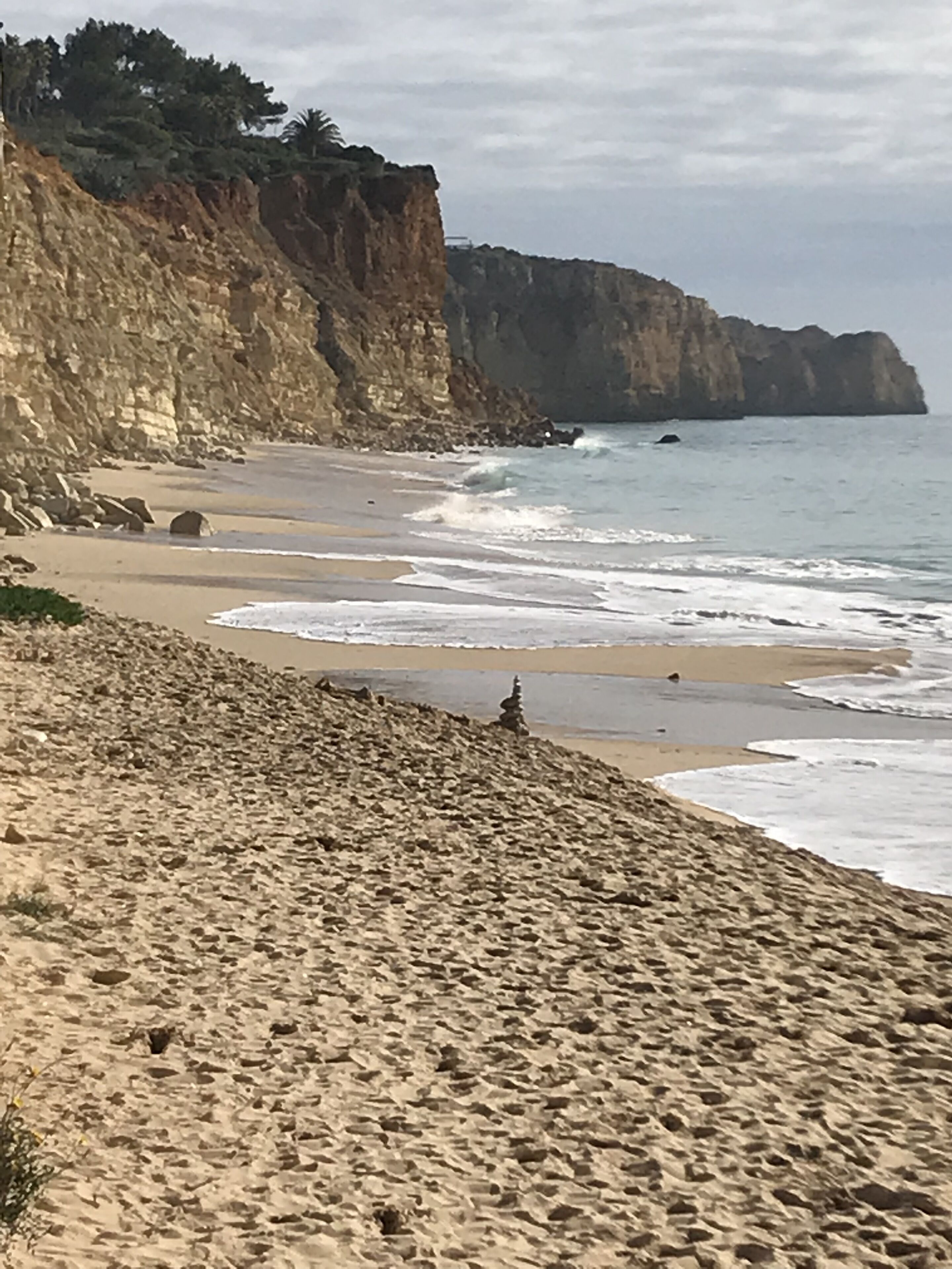 Una playa con un acantilado rocoso y olas rompiendo en la orilla.