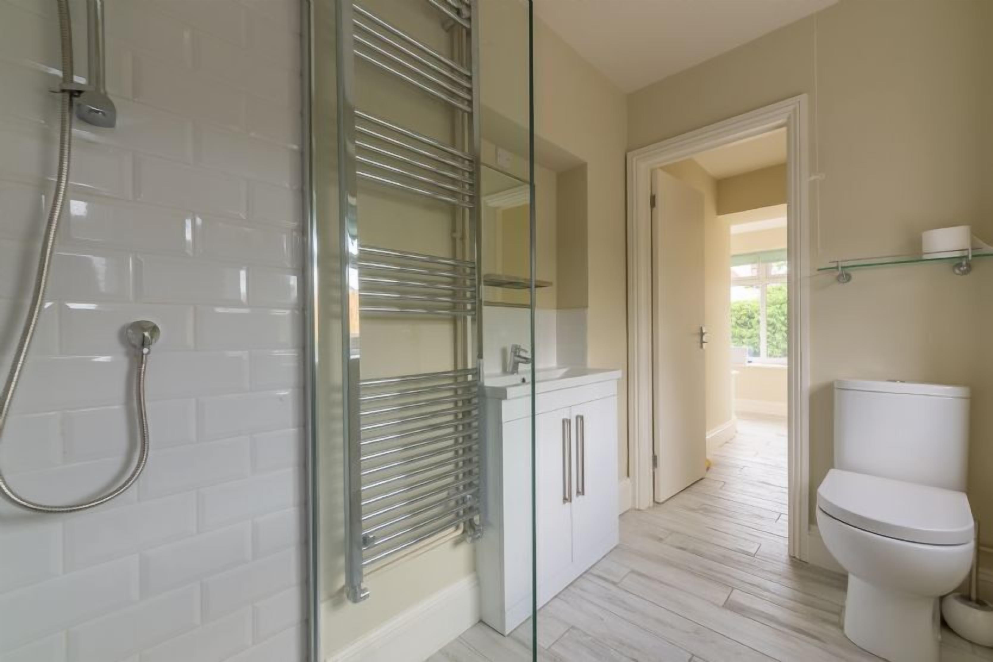 A modern bathroom with a glass shower enclosure, white tiles, a white toilet, and a glass shelf with toiletries.
