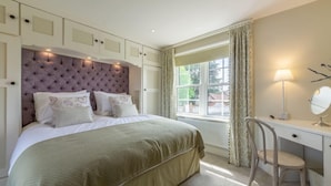 Un dormitorio con una cama grande, un escritorio con silla, una ventana con cortinas y una lámpara de noche.