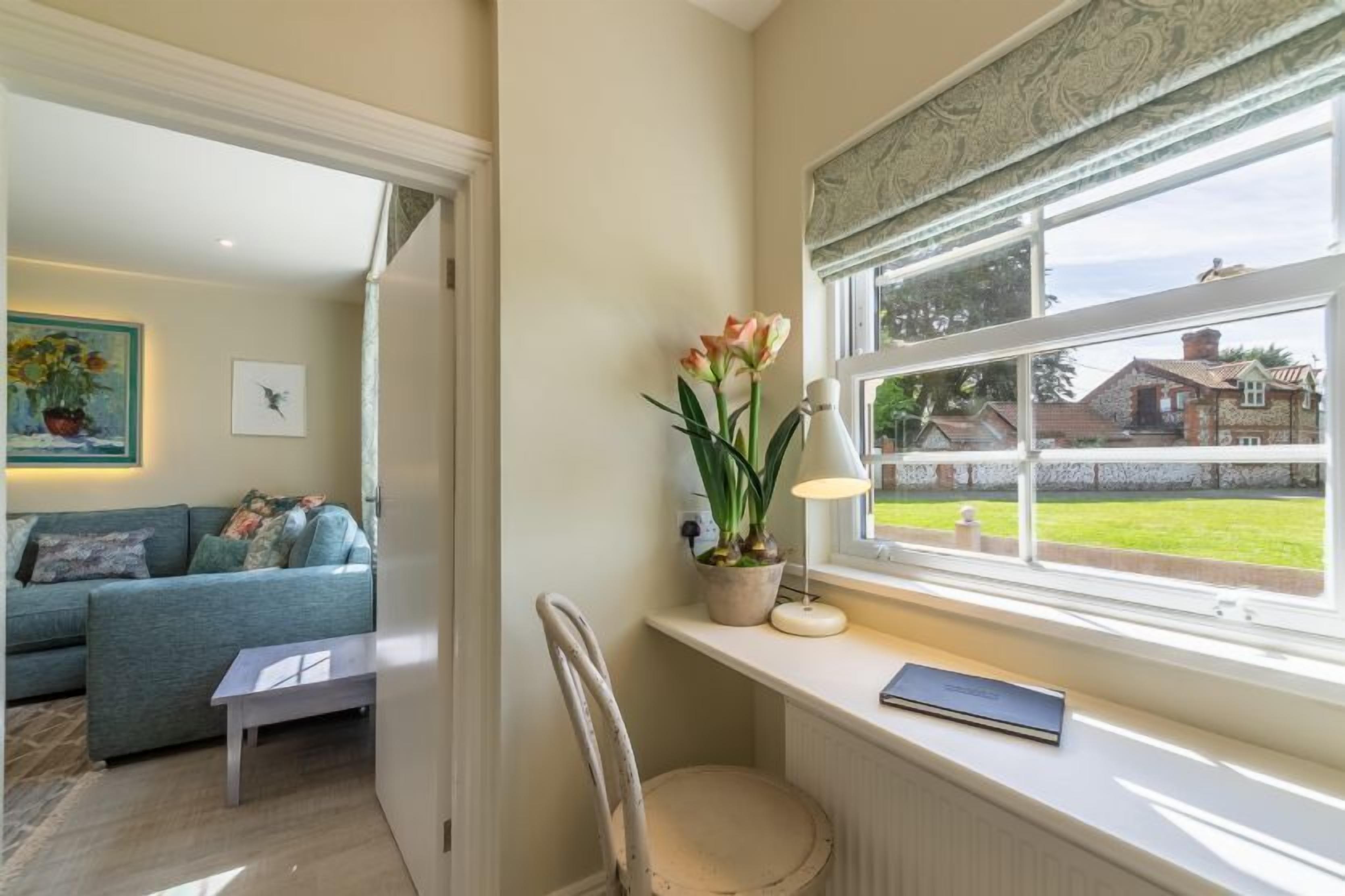Una sala de estar acogedora con un sofá, una mesita, una silla, una ventana con vistas a una casa y una planta en maceta.
