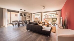 Ein geräumiger Wohnbereich mit einer Couch, einem Esstisch, Stühlen, großen Fenstern und einer roten Akzentwand.