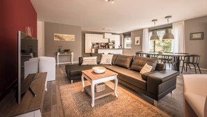Ein modernes Wohnzimmer mit Sofa, Couchtisch und Fernseher. Im Hintergrund ist eine Küchenzeile zu sehen.