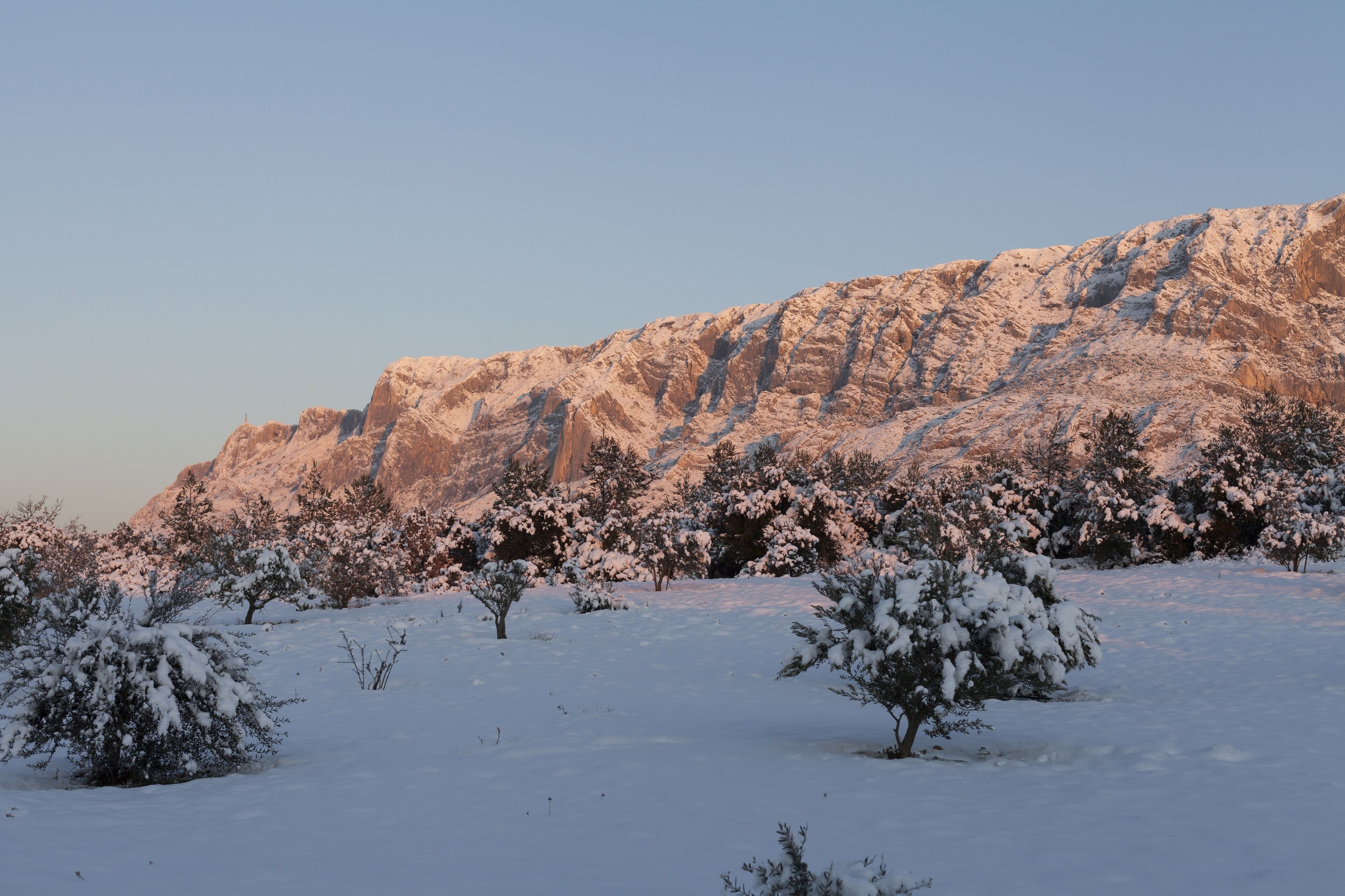 Eine verschneite Landschaft mit einem felsigen Berg im Hintergrund.