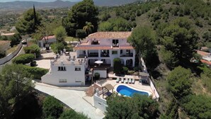 A large, two-story house with a swimming pool, surrounded by trees and hills.