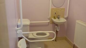 A small, private bathroom with a toilet, bidet, and a handrail.