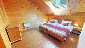 Puinen mökkimakuuhuone, jossa on kaksi sänkyä, pieni puinen kaappi, lämmitin ja kattovalokuvio.