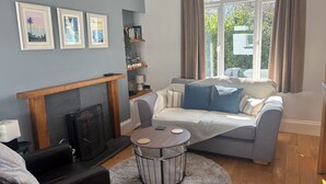 A living room with a fireplace, a sofa, a coffee table, and a bookshelf. - St Matthias Lodge - Delightful 2 bed cottage  (Torquay)