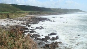 A coastal landscape with rocky shores and a grassy hillside. - Ideal location for families who like sandy beaches and dramatic coastal scenery (Gower)