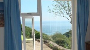 A room with a large window offering a view of a garden and the sea. - Ideal location for families who like sandy beaches and dramatic coastal scenery (Gower)