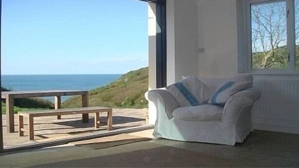 A room with a view of the sea, a white chair, and a wooden table. - Ideal location for families who like sandy beaches and dramatic coastal scenery (Gower)