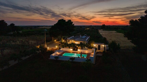 A house with a swimming pool, surrounded by trees and a sunset view.