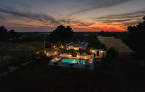 Une maison avec une piscine, entourée d’arbres et offrant une vue sur le coucher de soleil.