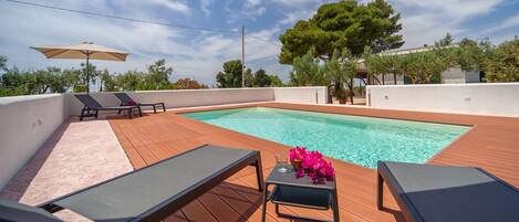 A rooftop pool area with lounge chairs and a table with flowers.