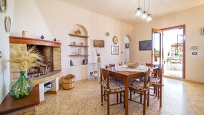 A dining area with a brick fireplace, wooden chairs, a table, and a chandelier.