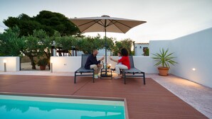 A poolside area with a wooden deck, a large umbrella, and a couple seated at a table.
