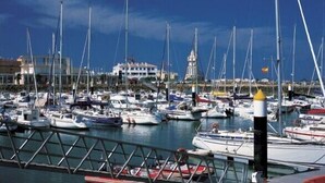 Un port de plaisance où sont amarrés de nombreux bateaux, une bouée jaune bien visible et, au loin, un bâtiment surmonté d’une tour.