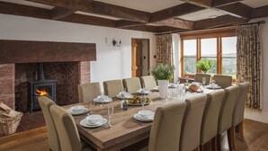 Uma sala de jantar com uma mesa de madeira posta para seis pessoas, rodeada por cadeiras, com lareira e vista para o exterior.