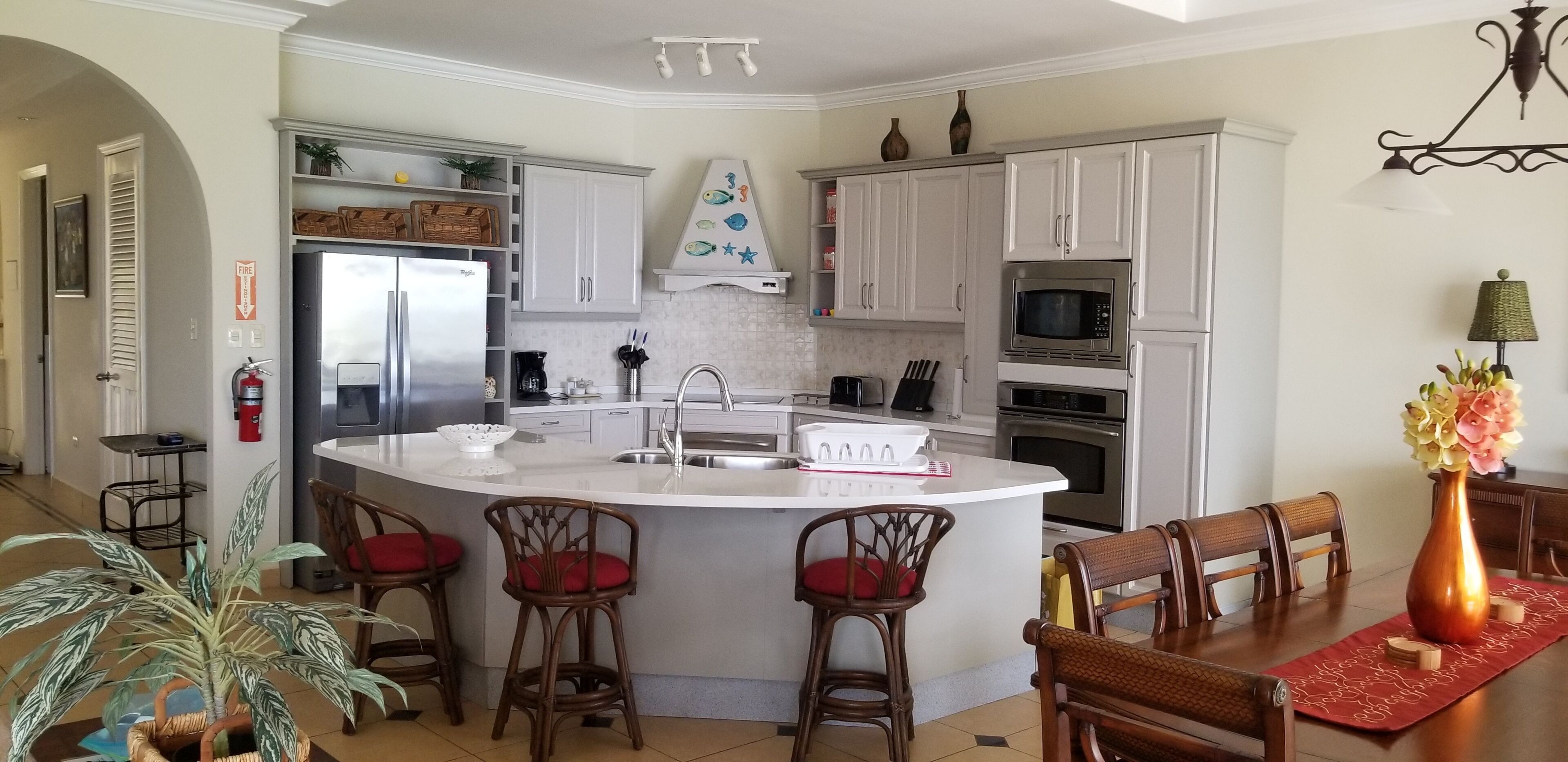 A modern kitchen with white cabinets, a central island with bar stools, a microwave, and a sink.