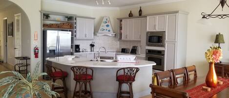 A modern kitchen with white cabinets, a central island with bar stools, a microwave, and a sink.