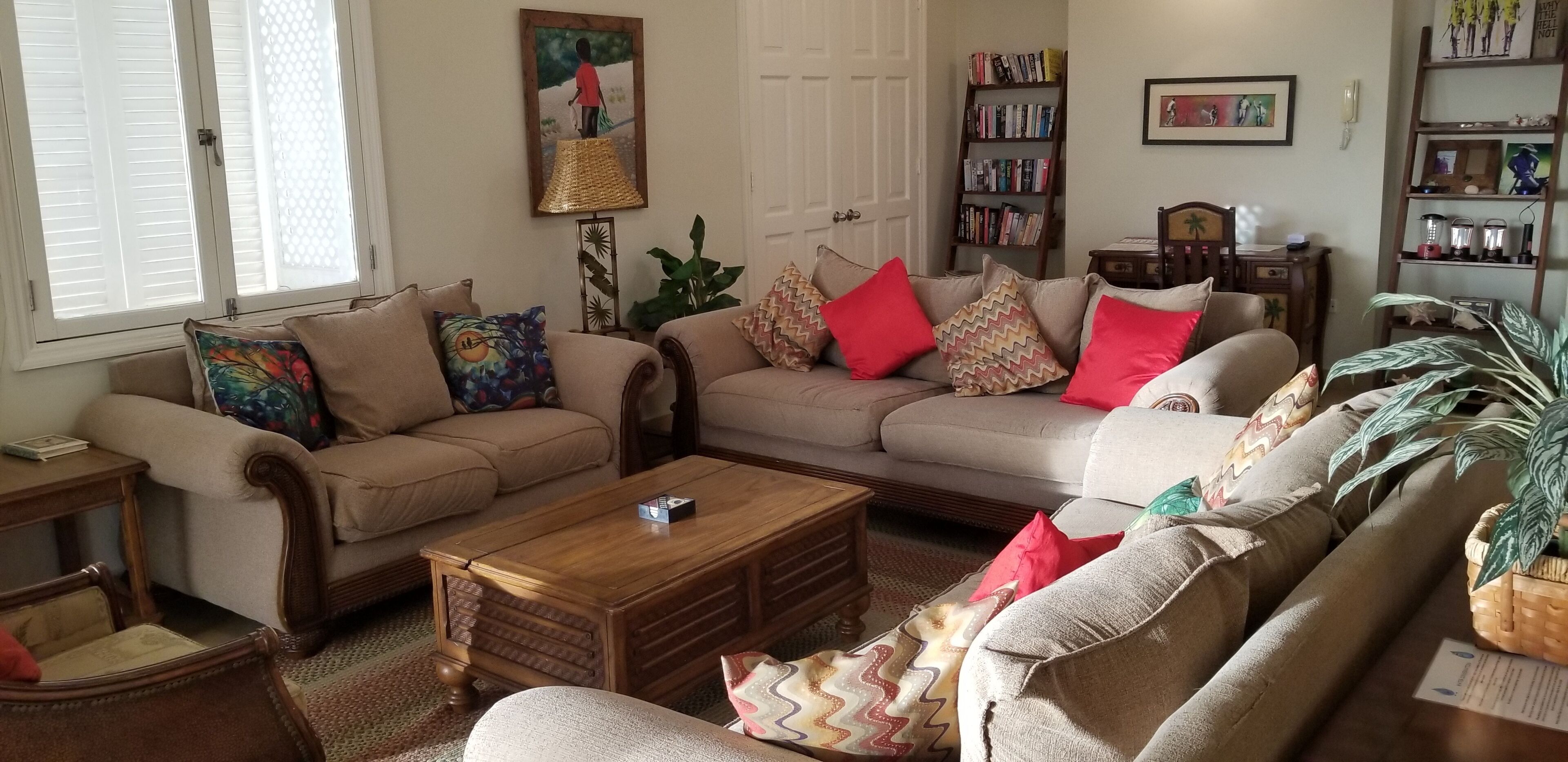 Een woonkamer met een beige zithoek, een houten salontafel, een boekenkast en een schilderij aan de muur.