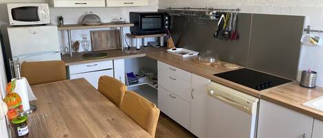 A compact kitchen with a microwave, toaster, kettle, and a stove. There is a dining table with chairs, a clock on the wall, and cabinets.