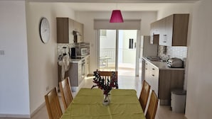 A dining area with a table set for six, a clock on the wall, and a kitchen in the background. - Beautiful Modern ,Apartment in Larnaca Area, Stunning terrace area & WIFI, Pools (Pyla)