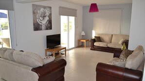 A living room with a sofa, a coffee table, a TV, and a painting on the wall. - Beautiful Modern ,Apartment in Larnaca Area, Stunning terrace area & WIFI, Pools (Pyla)