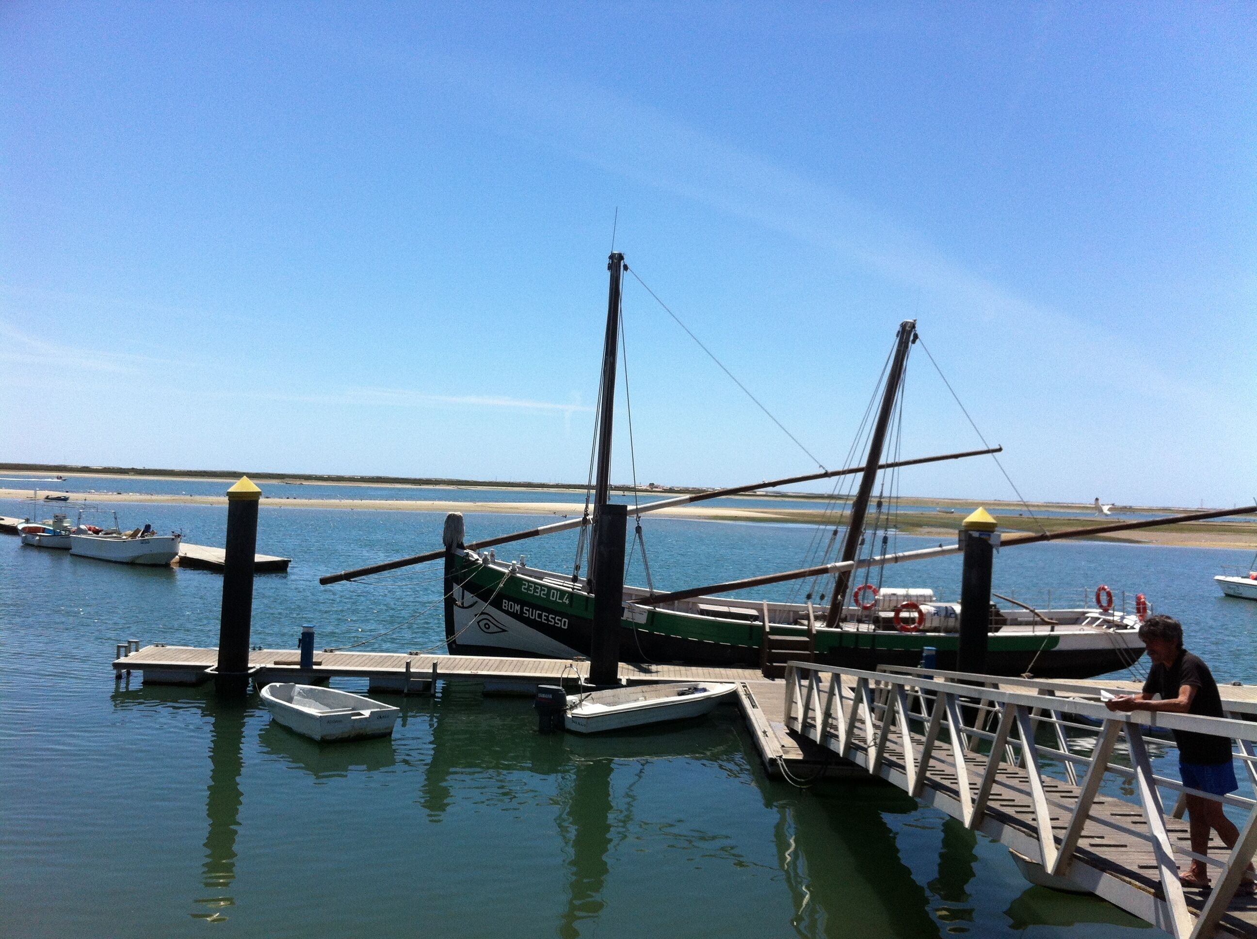 Un port de plaisance où sont amarrés plusieurs bateaux, une jetée et, en arrière-plan, une vue dégagée sur la plage.
