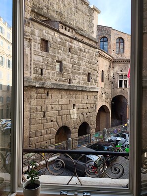 A view through a window of a stone building with arched doorways and a balcony railing. - Rome: House in the heart of the 'Roman Empire (Roma)