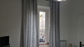 Ett sovrum med en säng, ett element, en lampa och ett fönster med gardiner.